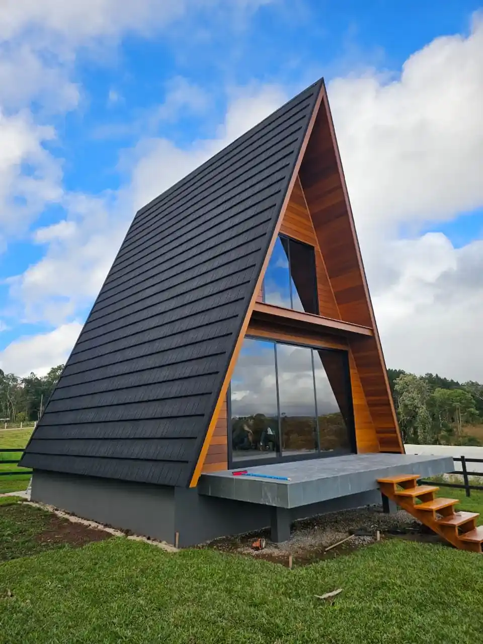 Chalé A-frame com cobertura Rock Steel Onix Black, fachada de madeira e grandes painéis de vidro.